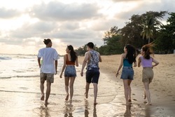 Group of Asian young man and woman having party on the beach together. Attractive friends singing and dancing while walking and running at seaside enjoy holiday vacation trip in tropical sea island.