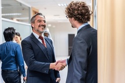 Caucasian businessman making a handshake together while stand in office. Attractive team of employee worker enjoy partnership agreement after negotiations for business deal during working in corporate