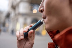 Close up of a man vaping with electronic cigarette outdoor on street. Attractive handsome male tourist travel alone on street, enjoy blowing the dense smoke out during walking in city town for holiday