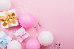 Pink table with balloons, gift or present box and confetti top view. Flat lay. Composition for birthday or party theme.