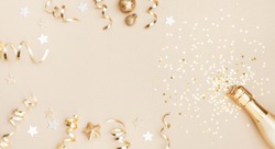 Champagne bottle with confetti stars, holiday decoration and party streamers on gold festive background. Christmas, birthday or wedding concept. Flat lay.