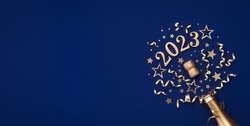 Festive Christmas and New Year background with golden champagne bottle, party decorations, confetti stars and 2023 numbers.