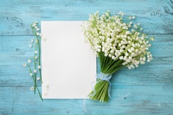 Bouquet of flowers lily of the valley and empty paper sheet on turquoise rustic table from above, beautiful vintage card, top view, space for text, flat lay.