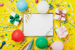 Party or birthday background. Frame with colorful balloon, gift box, carnival cap, confetti, candy and streamer on yellow table top view. Flat lay. Holiday mockup. Greeting card with copy space.