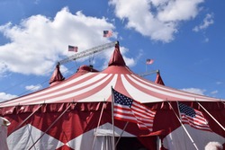 Red and white circus tent with American flags, blue sky