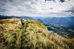 Female hiker walks along a ridge and enjoys the breathtaking view from the top of Loser mountain, Altaussee, Ausser Land, Salzkammergut, Styria, Austria