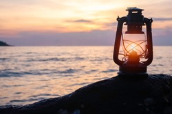 An old vintage oil lantern placing on a rock by the sea. It's evening time, the sun is setting. This is so romantic yet lonely scenery. The lamplight is used by fisherman. Chillout travel concept. 