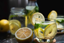Lemon detox infused water in clear glass on dark background.  Drinking organic lemon detox infused water for toxin cleansing is healthy. Detox infused water can boost vitamin and digestive system.  