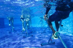 Fitness class doing aqua aerobics on exercise bikes in swimming pool resort hotel