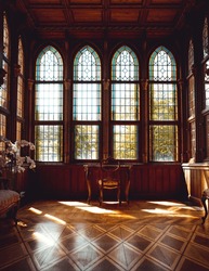 Sun shining into an old wooden room with high, beautiful windows and a single table in the center in a castle