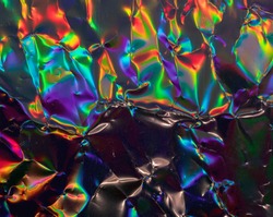 high res full frame macro photo of abstract crumpled iridescent holographic foil background with light leaks. holo color wrinkled material. cool glitter surface with shiny rainbow color blocking feel.