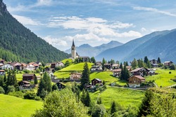 Beautiful Schmitten village at Albula pass in Grisons, Graubuenden, Switzerland with view of houses on green grassy hills, a lovely church on hilltop and majestic mountains in background