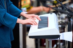 Musician woman playing on white synthesizer keyboard piano keys, focus on female hands on synthesizer. Musician playing musical instrument on concert stage, cropped image of person playing synthesizer