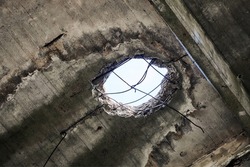 Vintage abandoned damaged house roof with hole in ceiling overlooking cloudy sky. Collapsed concrete wall with hole in abandoned industrial or residential building, close up