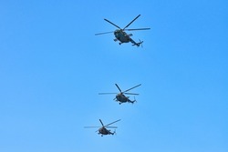 Three military helicopters flying in bright blue sky while performing demonstration flight, copy space. Aerobatic team performs flight at air show