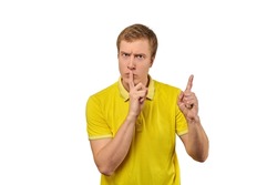 Funny male in yellow T-shirt asking to be quiet, silence gesture isolated on white background. Young man saying Shhh, keep quiet, please and making silence gesture, request for silence