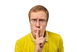 Funny young man in yellow T-shirt asking to be quiet, silence gesture isolated on white background. Young man in glasses saying Shhh, keep quiet, please and making silence gesture, request for silence