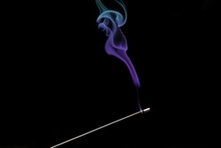 Smoke curls from burning incense stick for relaxation and meditation, black background. Aromatherapy session with burning aroma stick with turquoise purple smoke gradient color, pleasant aroma
