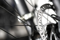 Bicycle disk brakes close up, grey metal disc attached to bike wheel, effective popular mountain bicycle brakes. Hydraulic disk brakes on bicycle wheel, bicycle spokes gray background