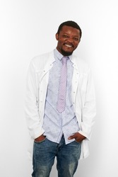 Happy black doctor man with small beard in white coat, bright shirt, tie and jeans, isolated on white background. Smiling adult black african american physician therapist half size portrait