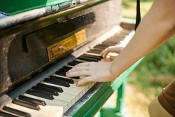 Female hands playing on old piano in public park, outdoor art music performance close up view. Playing on classic piano at outdoor concert green grass background