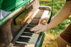 Female hands playing on old piano in public park, outdoor art music performance close up view. Playing on classic piano at outdoor concert green grass background