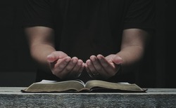 Men pray from god blessing to have a better life. Christian Crisis Prayer to God.  Men's hands praying to God with the Bible.  believe in good  Hold hands in prayer on a wooden table.