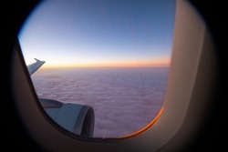 sunset horizon view from window seat in airplane in flight flying high above the purple fluffy clouds airplane wing and window frame in sight horizontal format room for type framed area air travel 
