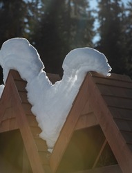 snow in angled wooden shingled triangular roof of sign shaped like the letter v backlit showing layers of snow in winter sun shining through snow vertical backdrop snakelike snow shape white and brown
