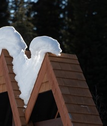 snow in angled wooden shingled triangular roof of sign shaped like the letter v backlit showing layers of snow in winter sun shining through snow vertical backdrop snakelike snow shape white and brown