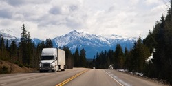 large white transport truck travelling on trans Canada highway in British Columbia Canada with scenic mountains mountaineous scenery in background good winter road conditions horizontal format 