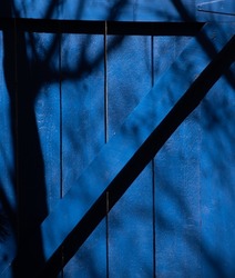 shadows of trees cast onto blue gate or door of home in afternoon slight black shadows on blue vertical format room for type wood frame triangular shape with vertical wood slats painted deep blue 