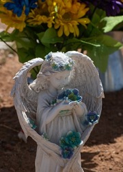 ceramic angel with wings holding blue flowers at side of road at gravesite memorial of accident victim along highway religious symbol of caring in memory of and heaven vertical format room for type 