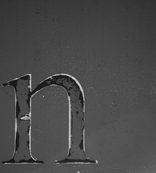 black and white photo of the letter small n isolated on side of rusty metal shipping container with peeling paint rust spots and paint chips grungy looking letter n with grey backdrop vertical format