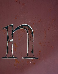 The small letter n isolated on side of rusty metal shipping container with red  burgundy or rust colored paint chipped weathered and grungy looking with peeling paint and rust spots vertical format 