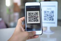 Women's hand uses a mobile phone application to scan QR codes in stores that accept digital payments without money and plastic tags on the table. QR code payment and cash technology concept