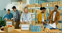 Caucasian and African American people men and women volunteers working at charity organization packing clothes and food grocery in donations box. Volunteering, social help for poor and needy