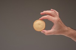 Single shortbread biscuit held by male hand. Close up studio shot, isolated on brown background.