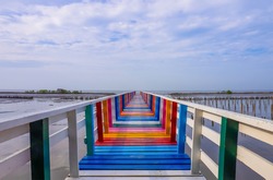 Rainbow bridge in Thailand. View of The colorful wood bridge extends into the sea under blue sky with white clouds at samut sakhon province,Thailand. Selective focus.

