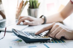 Close up Business woman using calculator and laptop for do math finance on wooden desk in office and business working background, tax, accounting, statistics and analytic research concept