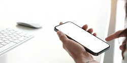 Mockup image blank white screen cell phone.women hand holding texting using mobile on desk at home office. 