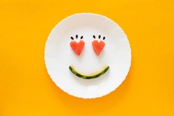 Smiling faces on a white plate on an orange background. Heart shape from watermelon. Smiling symbol. Concept enjoy eating. Summer time