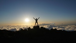 Hiker celebrates meeting beautiful sunset at a mountain peak above clouds at Haleakala Volcano in Maui, Hawaii 