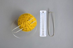 One skein of yellow wool yarn, knitting spokes, measuring ruler and large pin on gray background, handmade, knitting. Close-up. Copy space. Selective focus.