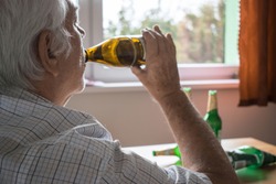 old senior man sit next to table drink alcohol bottle at home sad alone alcoholism