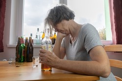 old senior female woman sit next to table drink alcohol bottle at home sad alone alcoholism Signs and Symptoms rehab abuse and recovery problems