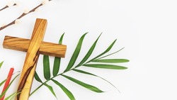 Easter religion composition with wooden crucifixion, palm leaf, willow branch and red church candle on a white background with copy space. The concept of Holy Week, Palm Sunday and Lent