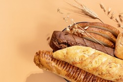 Homemade natural breads. Fresh loafs of bread in the blue basket with ears of rye and wheat on a beige background with copy space. Crunchy french baguettes, slices of bread and a bun. Soft focus 