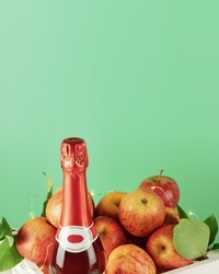 Apple wine or cider drink or fermented fruit drink. Bottle with cider and red organic apples in a white wooden box on a green background with copy space. Apple, low alcohol drink