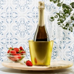 Summer holiday still life with bottle of champagne and fresh strawberries in a glass bowl on wooden podium opposite tile wall. Dating or love concept. Womans day, birthday, valentines day. Front view